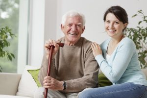 Elderly gentleman holding walking stick whilst seated on a sofa with their careworker